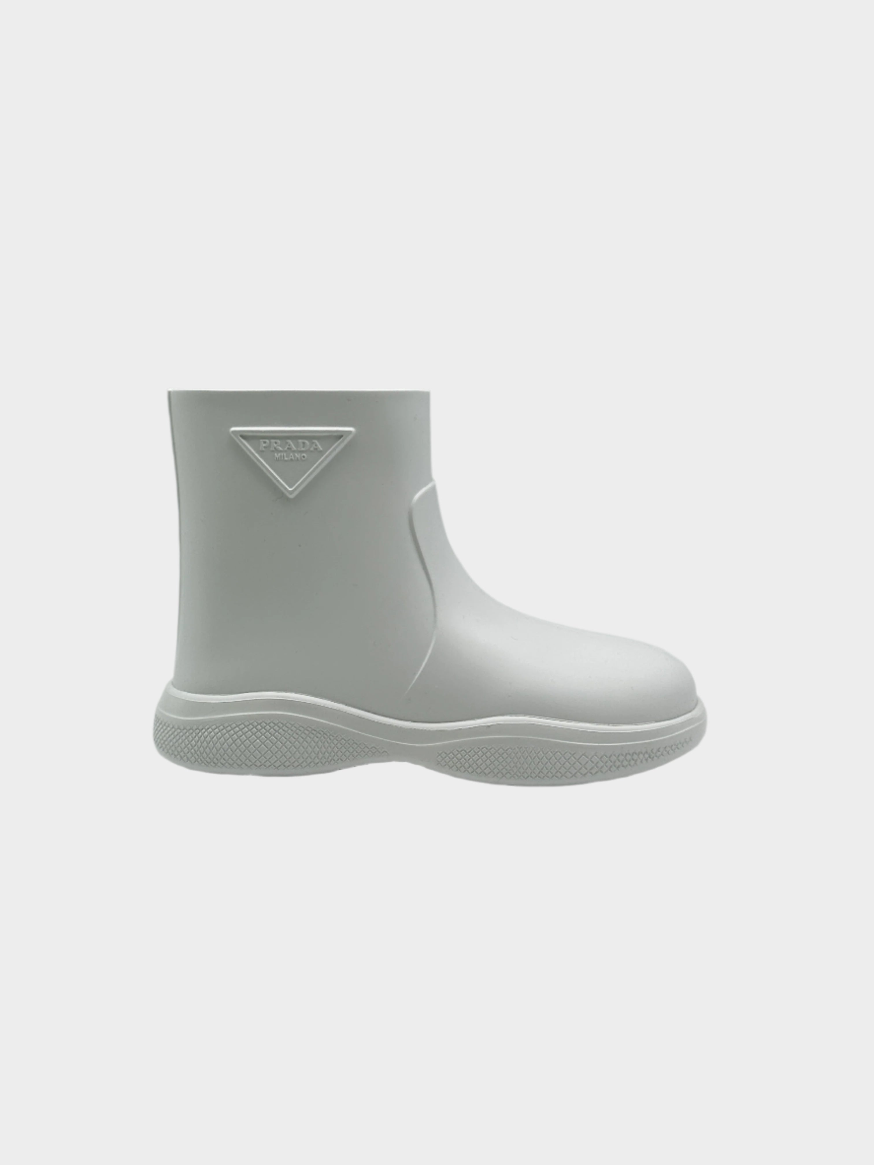 Stivali in gomma bianchi di Prada dal design minimal e moderno. Realizzati in materiale impermeabile con suola testurizzata per una maggiore aderenza. Caratterizzati dall'iconico logo triangolare in rilievo sul lato, questi stivaletti uniscono funzionalità ed estetica contemporanea.