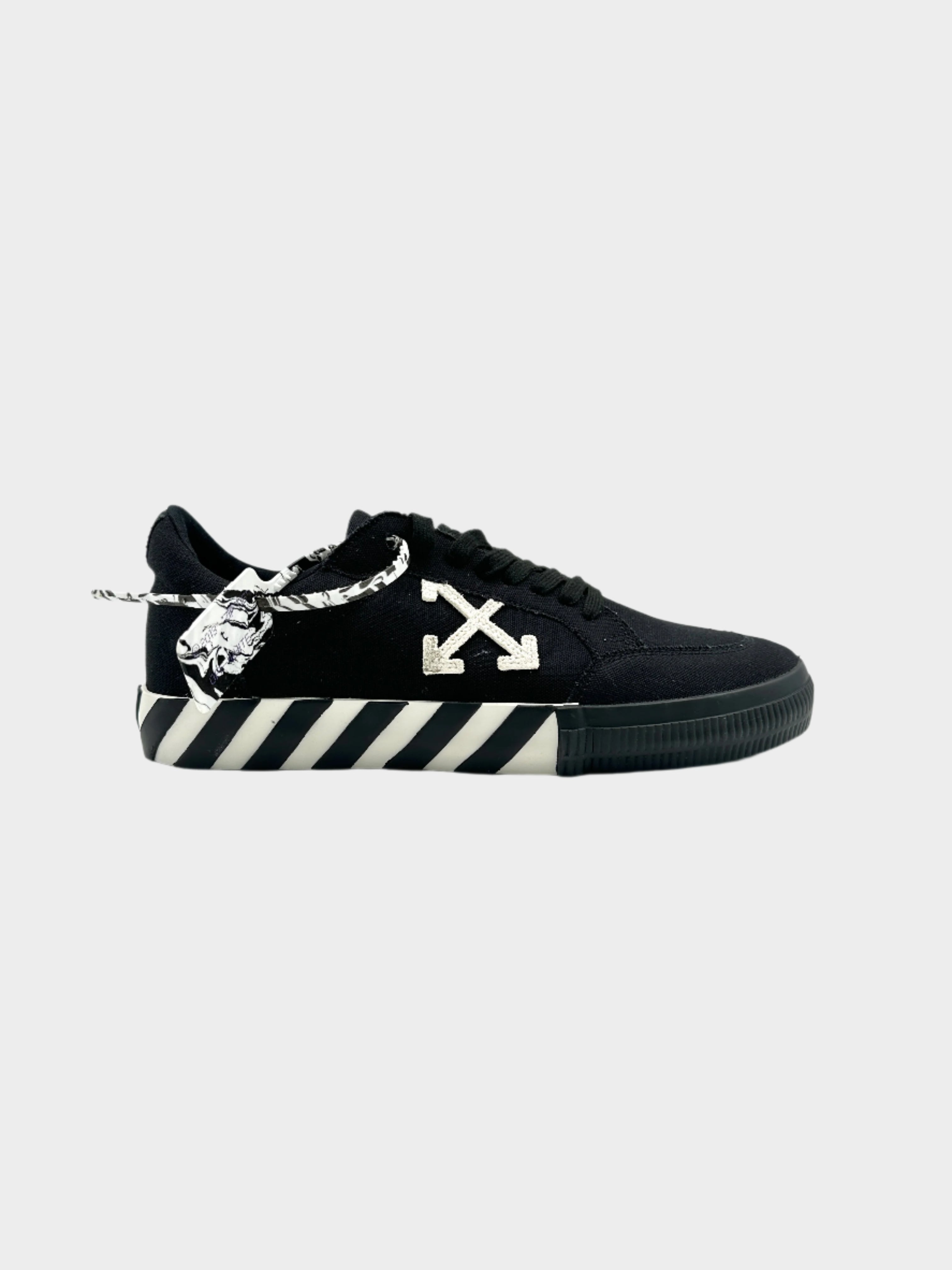 Sneakers basse Off-White Vulcanized nere. Logo a freccia bianco, suola con righe diagonali e zip-tie iconico. Stile streetwear audace e contemporaneo.