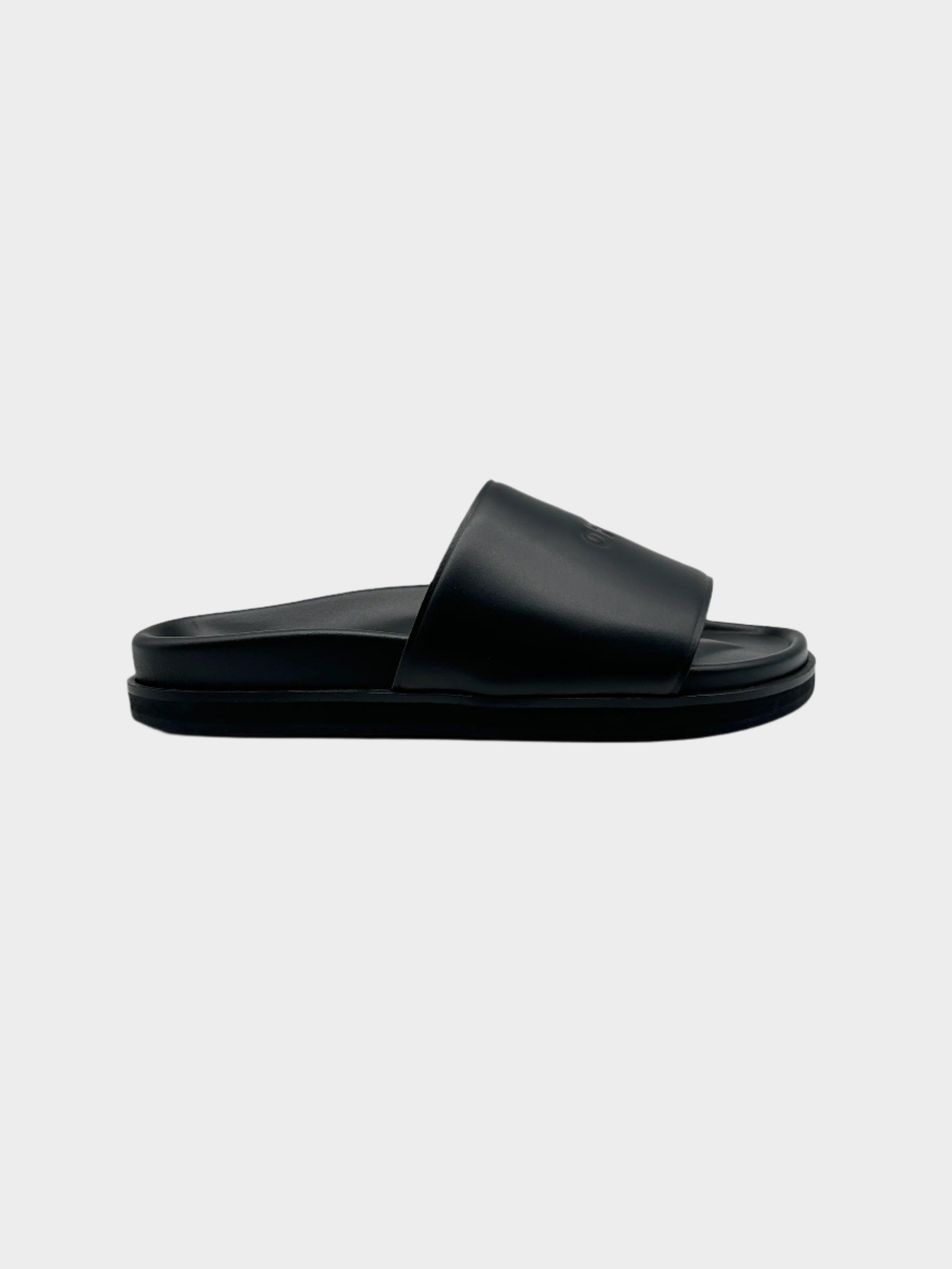 Slippers Off-White in gomma nera con fascia ampia e logo tono su tono. Design minimal e confortevole, perfette per un look casual e contemporaneo.