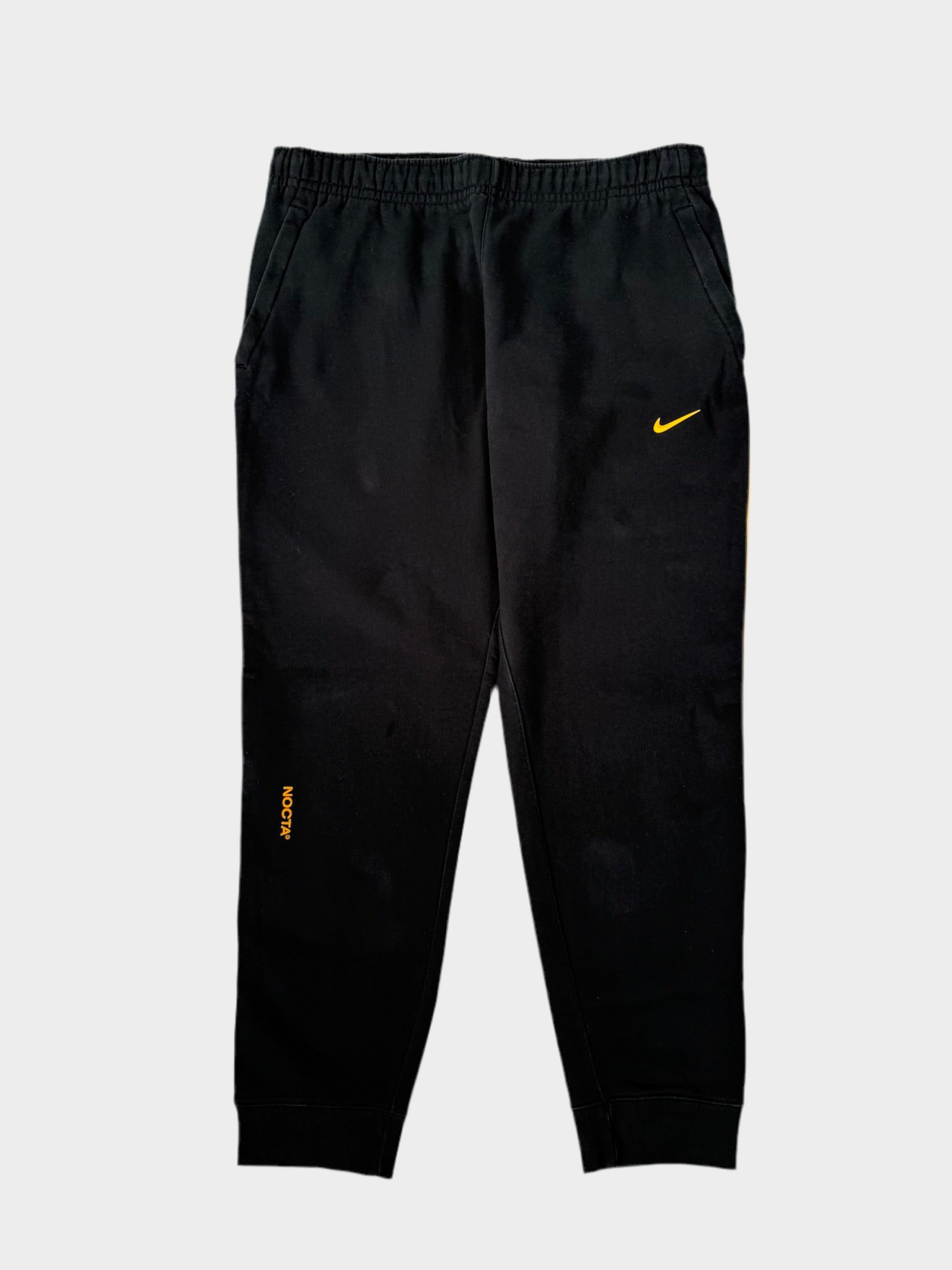 Vista frontale del pantalone della tuta Nike x Nocta nero con dettagli gialli
